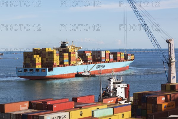 Maersk Serangoon cargo ship loaded with metal box shipping containers being guided by pilot boats