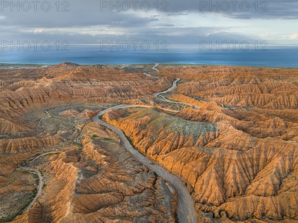 River bed runs through a landscape of eroded hills, badlands, Issyk Kul Lake in the background,