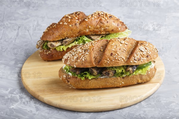Sprats sandwiches with lettuce and cream cheese on wooden board on a gray concrete background. side