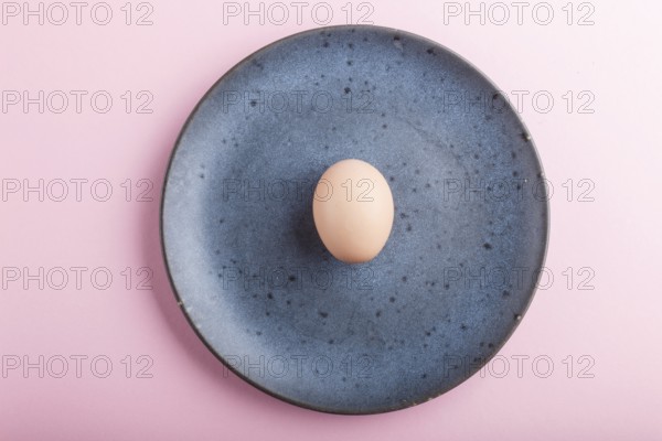 Raw uncooked single egg on a blue ceramic plate on a pink pastel background. top view, copy space