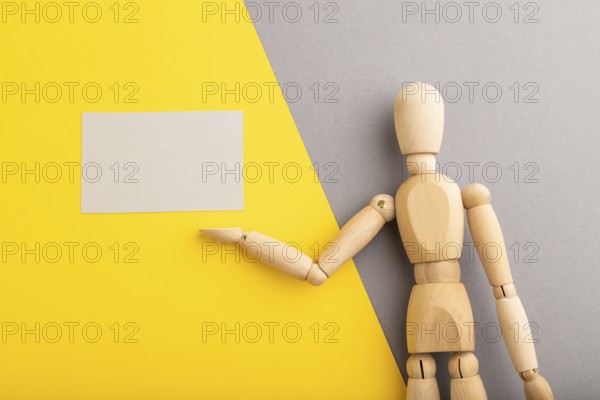 Wooden mannequin holding gray blank poster on gray and yellow pastel background. copy space,