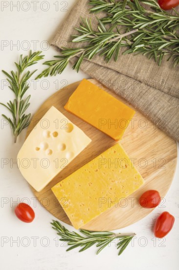 Various types of cheese with rosemary and tomatoes on wooden board on a white wooden background and