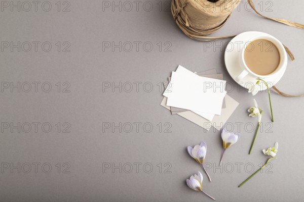 White paper business card mockup with spring snowdrop crocus and galanthus flowers and cup of
