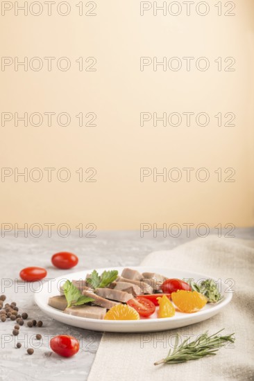 Boiled pork tongue with tomatoes and herbs on a gray and orange background and linen textile. Side