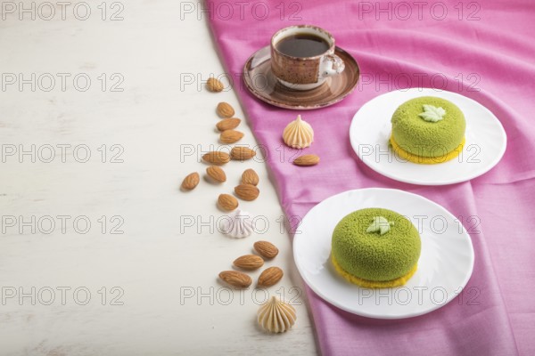 Green mousse cake with pistachio cream and a cup of coffee on a white wooden background and pink