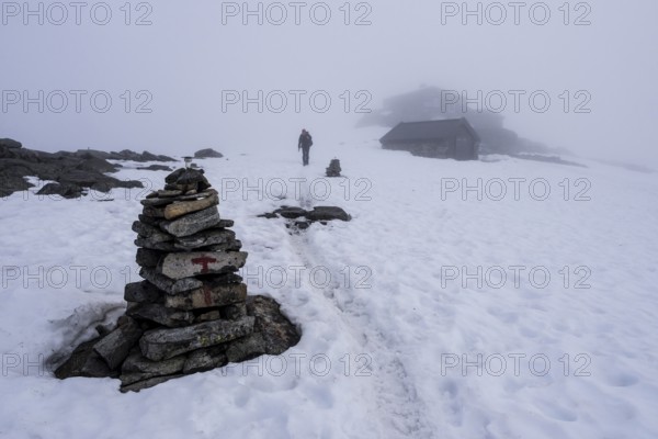 Path on snow between buildings on top of mountain Fannaråken, fog, signpost, single hiker,