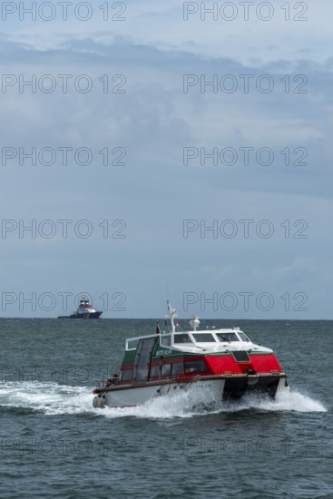 Dune ferry full speed ahead to the offshore island of Helgoland, tugboat on the horizon, North Sea,