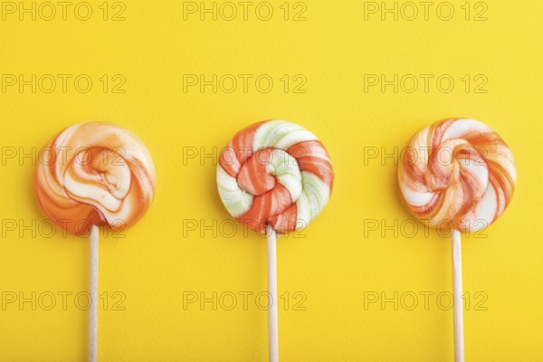 Three lollipop candies on yellow pastel background. copy space, top view, flat lay