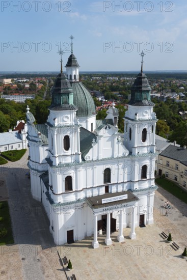 Large baroque church with white facades and green towers in a cityscape in sunny weather, Basilica