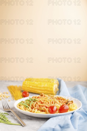Corn noodles with tomato sauce and arugula on a gray and orange background and blue textile. Side