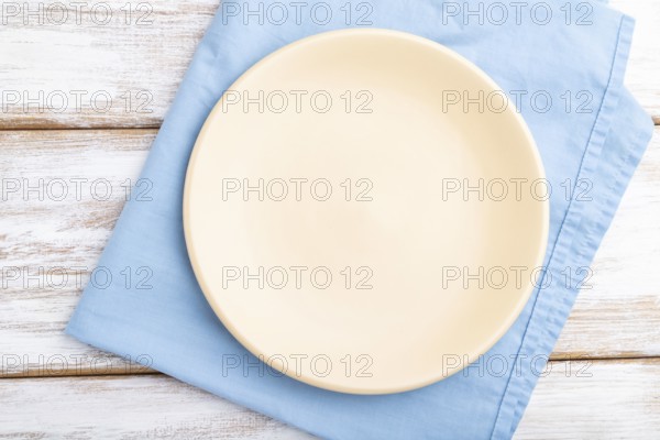 Empty ceramic plate on white wooden background and blue linen textile. Top view, close up, flat lay