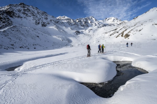 Small stream in a snow-covered mountain landscape, ski tourers in a valley, ascent to the