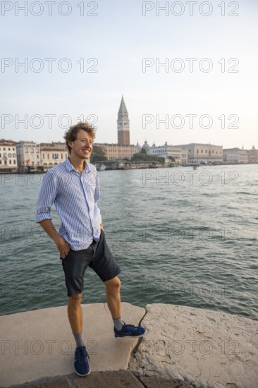 Young man in striped shirt and shorts on the banks of the Grand Canal, behind Campanile, Venice,