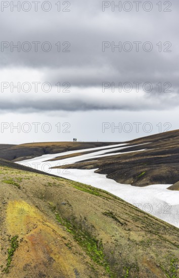 Two hikers on a hill in the distance, colourful volcanic landscape with hills and snow, Laugavegur