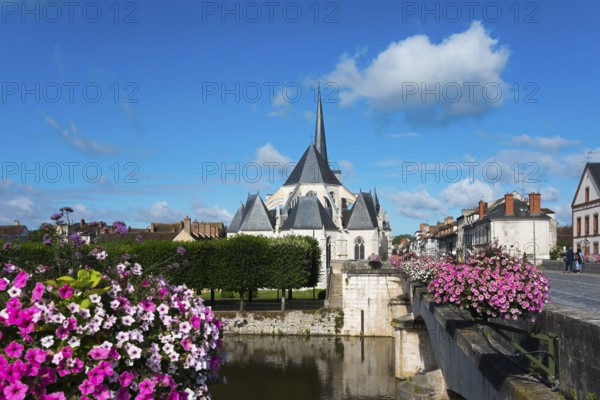 Ansicht einer Kirche in einem kleinen Dorf mit blauen Himmel und weißen Wolken, umgeben von Blumen