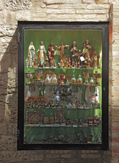 Shop window with figures of saints, devotional objects, in the historic centre of Assisi, Umbria,