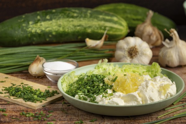 Ingredients for tzatziki, garlic, grated cucumber, sour cream and chives on a plate