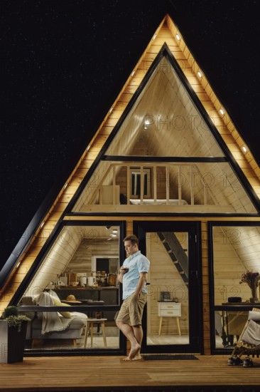 Man with a glass in his hand standing on terrace of tiny house at late evening and enjoys calmness