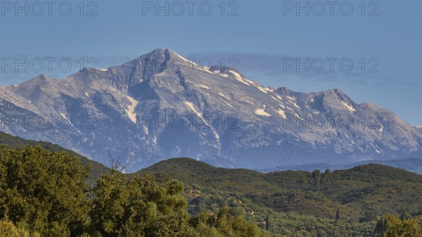 A majestic, snow-capped mountain peak rises above green forests, Taygetos Mountains, Mani