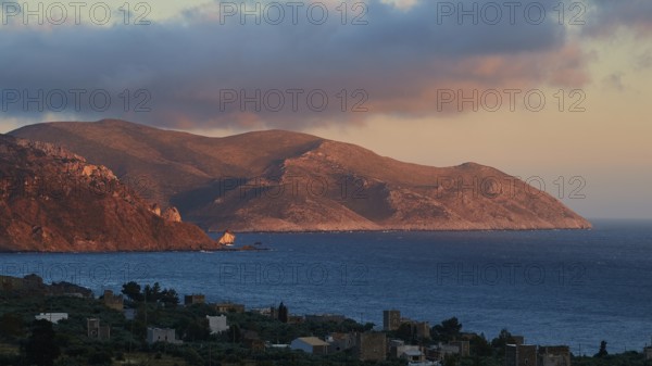 A mountain landscape at dusk with a view of the sea and a small settlement in the foreground, Mani