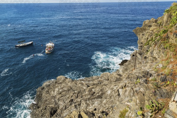 Rocky cliff and fishing boats moored in bay, Ligurian Sea, Manarola village in late summer, Cinque