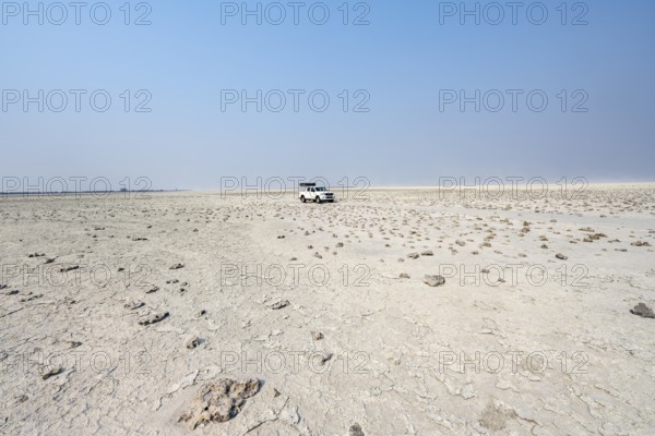 Four-wheel drive Toyota Hilux with roof tent, driving over salt pan, lone car in large wide plain,