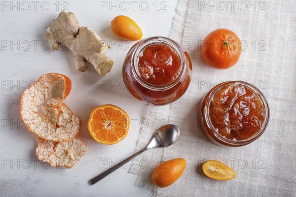 Tangerine and kumquat jam in a glass jar with fresh fruits on white wooden background. Homemade,