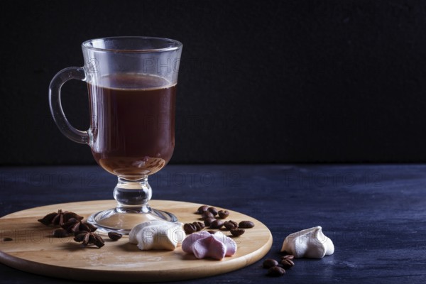 Glass cup of coffee with meringues on a wooden board on a black background. close up, copy space