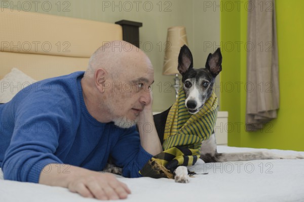 A mature gentleman, accompanied by his greyhound companion, poses for the camera from the comfort