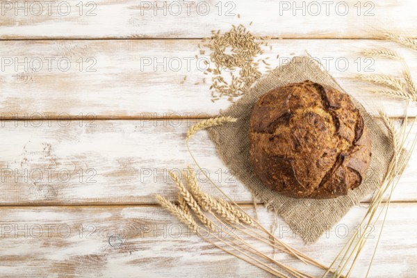 Fresh homemade golden grain bread with ears of wheat and rye on white wooden background and linen
