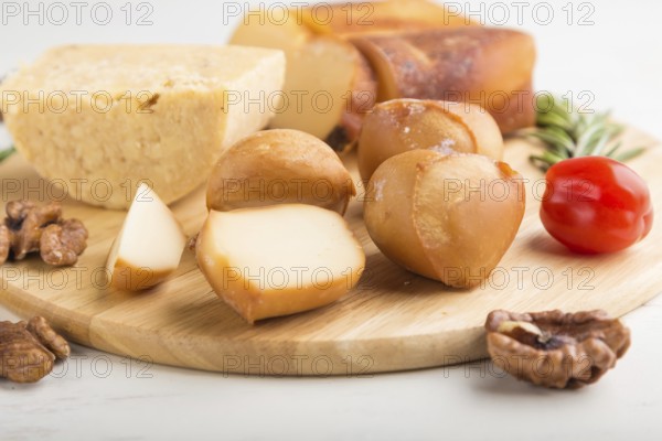 Smoked cheese and various types of cheese with rosemary and tomatoes on wooden board on a white