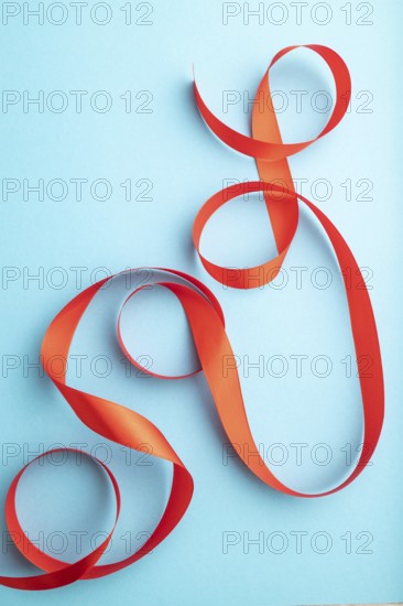 Red coral ribbon on a blue pastel background. Celebration concept. Top view, close up, flat lay