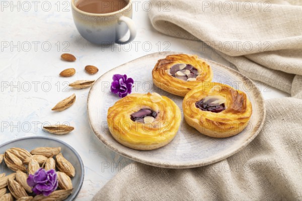 Small cheesecakes with jam and almonds with cup of coffee on a white concrete background and linen