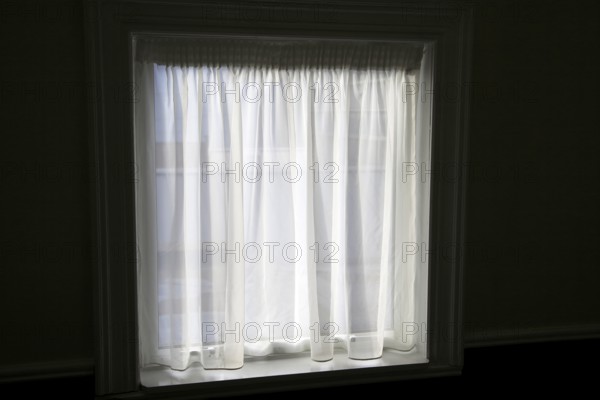 Net curtain in window of dark room letting in light