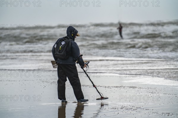 Treasure hunter, man with metal detector on the beach, dark storm clouds, autumn at the North Sea