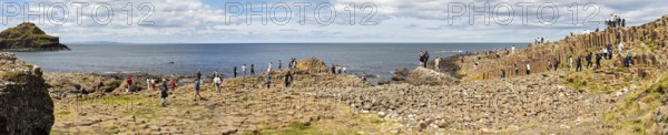 Panorama of people on basalt columns with sea view under cloudy sky, Giant Causeway