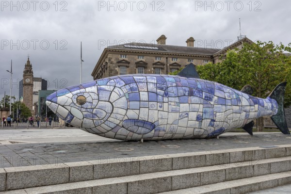 Colourful fish sculpture made of tiles in a public square in front of a historic building, Belfast