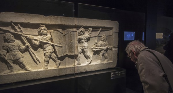 Visitor looking at tomb relief fragment showing gladiators fighting in ancient Rome in the