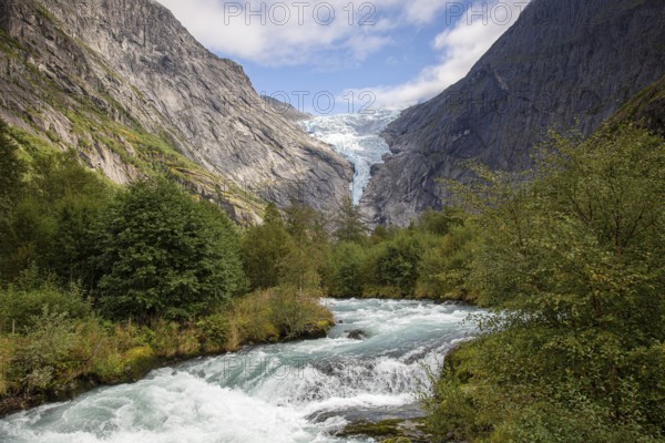 A river flows in front of the melting Kjenndalsbreen glacier between steep mountains through a