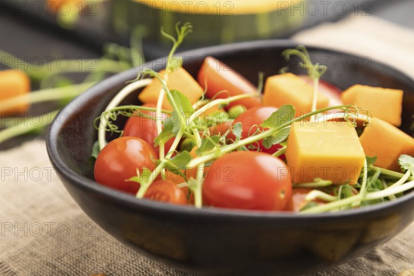 Vegetarian vegetable salad of tomatoes, pumpkin, microgreen pea sprouts on black concrete
