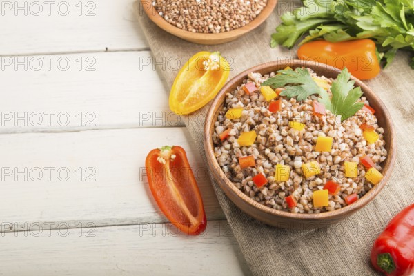 Buckwheat porridge with vegetables in wooden bowl on a white wooden background and linen textile.