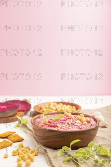 Hummus with beet and microgreen basil sprouts in wooden bowl on a white and pink background and