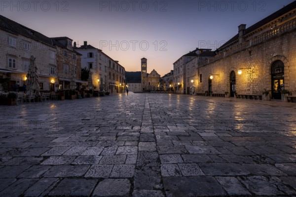 Old town square with cobblestones and illuminated ancient buildings at sunrise, Hvar, Croatia,