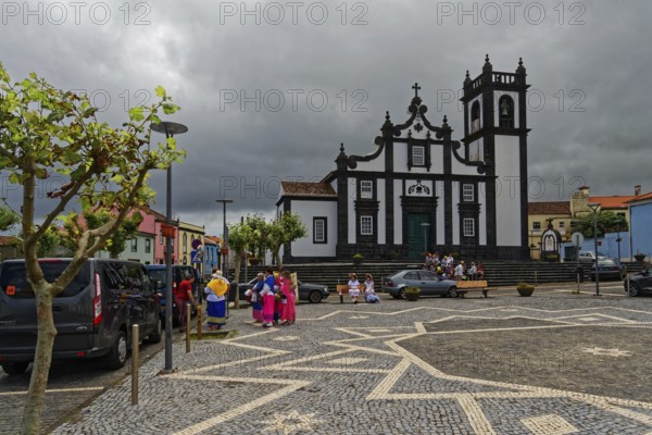 Square with historic church Nossa Senhora da Luz in the background, people in traditional dress,