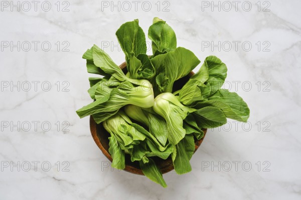 Vibrant green bok choy is neatly arranged in a rustic wooden bowl, set against a clean marble