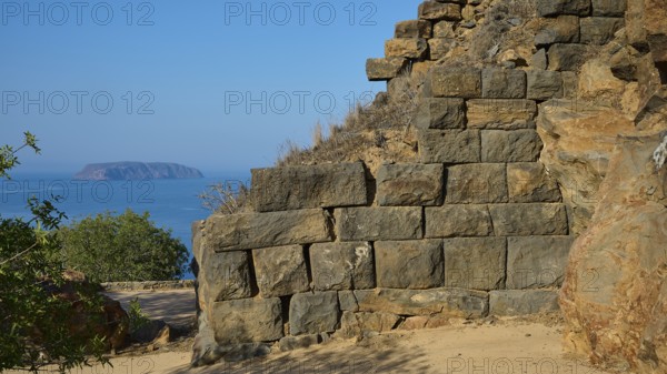 Ancient stone structures against a clear blue sky with the sea in the background, Palaiokastro,