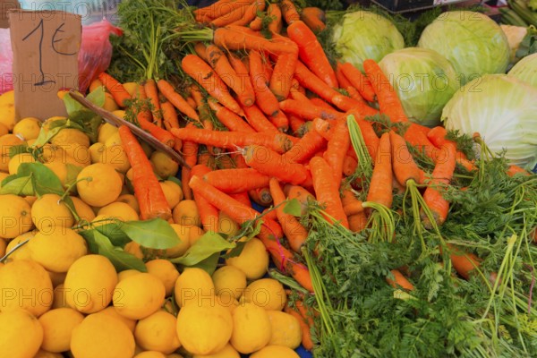 Market stall with fresh vegetables such as carrots, lemons and cabbage. A price tag shows the price