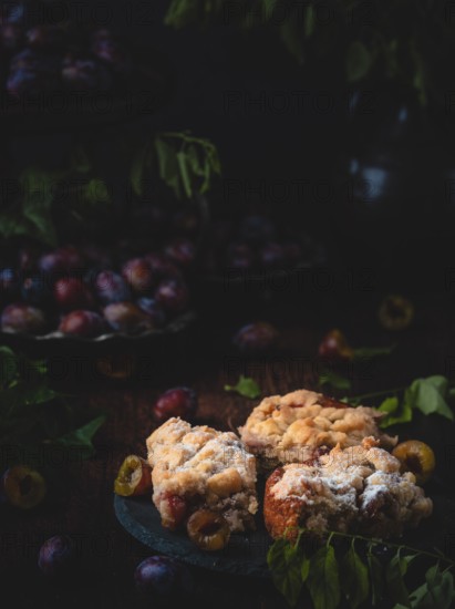 Plum cake on a plate in a dark, cosy, autumnal setting with plums and leaves