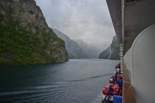 A cruise ship, my ship 6, sails through a misty fjord surrounded by green mountains and waterfalls,