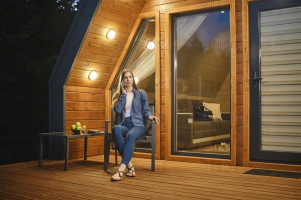 Late at night a girl sits on the terrace of a tiny house and talks on the smartphone with her